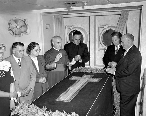 "Archbishop Hanna. Stateroom and afternoon on ship. SS PRES. MONROE. Aug. 18 '47. A. Sponagel" Funeral rites on deck and in cabin. On-deck service appears to be ritual following mass, and is attended by many clergy & large crowd, including photographers. Interior shots show small group around draped casket; priests are not wearing vestments for mass. Other shots show casket coming aboard. Not all negs are #'d. Unassigned