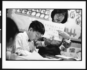 Woman holds flashcard with Korean writing on it while students take notes, Oriental (Los Angeles), 1996