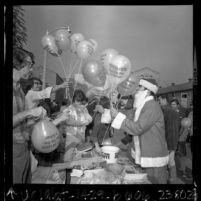 Man in Santa Claus outfit handing out balloons printed with "Peace on Earth Stop The War In Vietnam" in Los Angeles, Calif., 1967