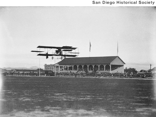 People watching an early airplane fly over the Coronado Polo grounds during an air meet