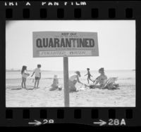 "Quarantined…Polluted Water" sign with children playing in sand behind it on Cabrillo Beach, Calif., 1973