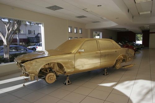 The Jewel / In God We Trust: junk car covered in gold leaf in luxury car dealer showroom