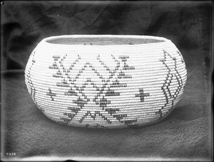 Indian basket displayed in front of a cloth backdrop, ca.1900