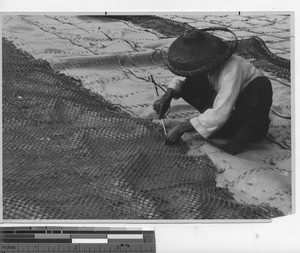 A woman mending a fishing net at Wuzhou, China, 1936