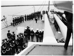 Officer reading to sailors and Marines in a ceremony on the deck of a battleship