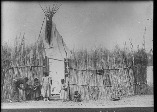 Kiowa Indians with tepee and grass stockade