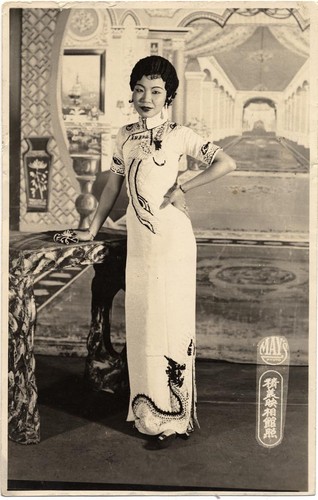 Actress in cheongsam decorated with dragon and phoenix poses hand on hip and leaning on a table /