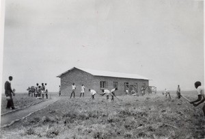 Young African men weeding weed around a building of the Libonda upper school