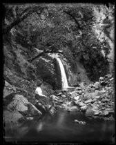Woman seated on rocks, looking at waterfall
