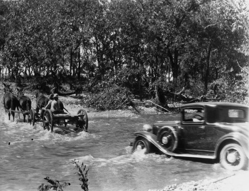 Four Horses and Wagon Pulling Automobile Across Stream [graphic]