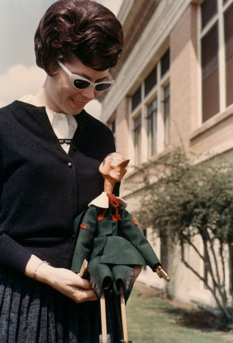 Judy Huey Standing with Pinocchio Doll Next to Anaheim Public Library, Carnegie Building [graphic]