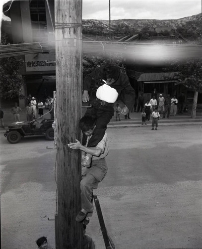 People assisting a man an hanging from rope harness on utility pole