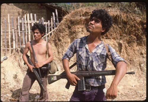 Two armed guerrilleros in civilian clothes stand in the countryside, La Palma, 1983