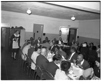 Woman holding coffee pot as group is seated at dining tables, Holland guild #5