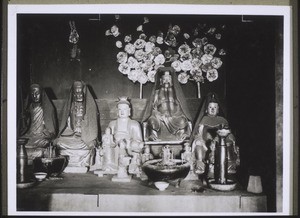 A row of deities in a temple in the vicinity of Kayin. In the foreground vessels for incense, in the background paper flowers