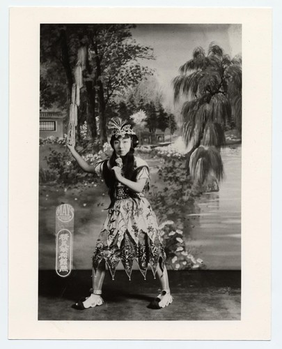 Actress in classical costume of celestial personage carrying a whip and with "ear-muff" hairdo /