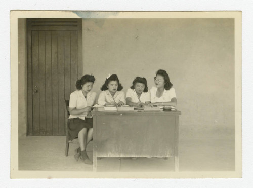 Nisei women working at desk in front of barrack