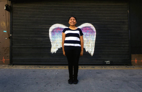 Unidentified woman in a striped shirt posing in front of a mural depicting angel wings