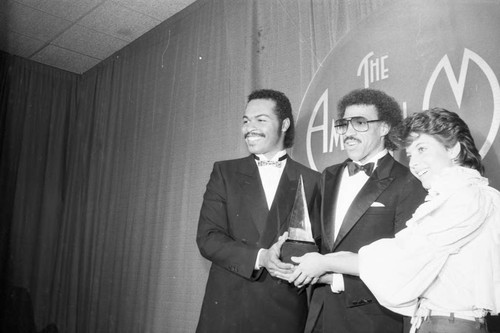 Ray Parker, Jr. and Moon Zappa posing with Lionel Richie at the American Music Awards, Los Angeles, 1983
