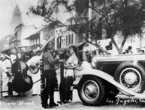 Photograph of Olvera Street- man and woman and old car at Macy Street entrance looking toward City Hall