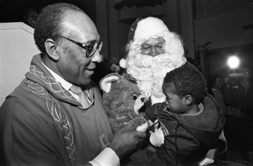 Rev. H.H. Brookins with Tom Bradley in a Santa suit talking to a child, Los Angeles, 1982
