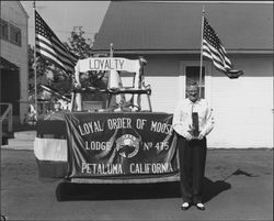 Man holding a trophy standing next to a float of the Loyal Order of Moose, Petaluma, California, about 1956