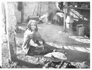 Yuma Indian woman sitting by her cooking fire in the ramada of her native dwelling, ca.1900
