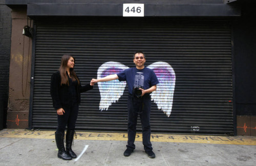 Unidentified man and woman holding hands and posing in front of a mural depicting angel wings