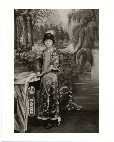 Actress wearing everyday ornate patterned silk dress of 1910s style with wide sleeves, a "cloche" hat and high-heeled black leather patent shoes /