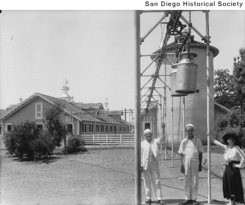 Two men and a woman standing beneath milk cans at the Dupee Dairy