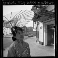 Takako Hoshiba with parasol walking down street during Los Angeles' Little Tokyo renewal efforts, 1965