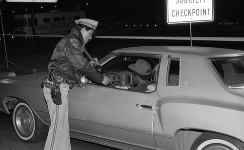 Los Angeles County sheriff's deputy talking to a motorist at a field sobriety checkpoint, Los Angeles, 1985