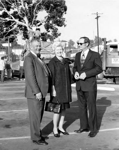 Two men and a woman posing in front of a tree planting