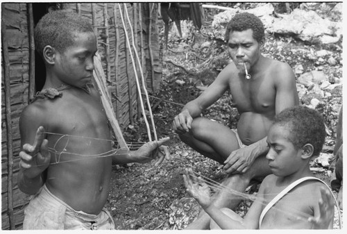 Laete'eboo and his sons playing with lalefui'olanga string figures in front of the men's house