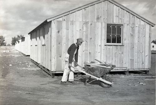 Man with wheelbarrow in front of labor camp buildings