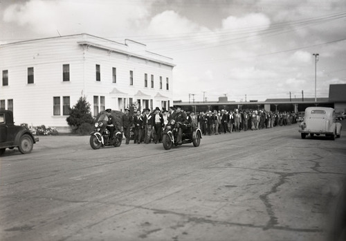 A large group of Mexican workers walking down a street with a police escort