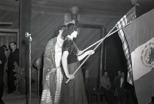 Two women holding Mexican and American flags