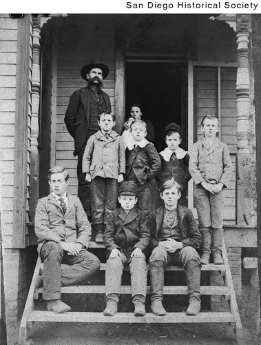 A man and woman standing on a porch behind seven boys on the steps