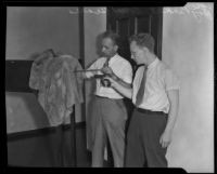 Ray Pinker and Robert Seares examine a bullet hole in a coat, Los Angeles, 1929-1939
