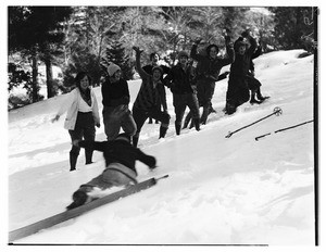 Group of people in winter gear smiling and waving while one of them falls down onto the snow at Big Pines