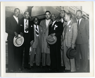 Joe Louis (center) and Frederick M. Roberts (fourth from right) standing with a group of unidentified men in front of airplane
