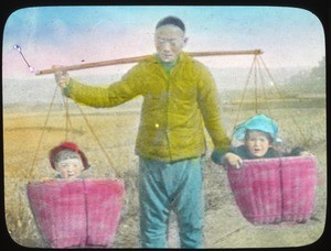 Man carrying two young children in the baskets of a yoke, China, ca.1917-1923