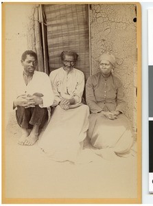 Two African men and one woman sitting in front of a hut, South Africa
