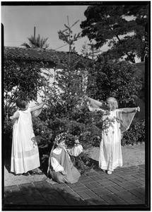 Three girls decorating a small Christmas tree with ornaments outside a home