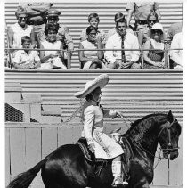 View of Flor Silvestre as she sings and performs on her horse during the rodeo at the California State Fair. Governor Ronald Reagan and his family sit in the grandstand. On Reagan's left is the wife of the Executive Secretary for the fair, Mrs. William P. Clark. This was the last fair held at the old fair grounds