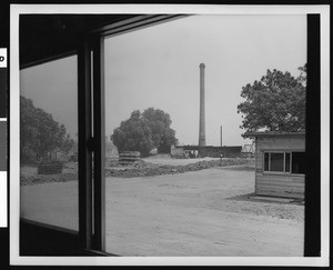 Exterior of an unidentified factory, showing the outlines of a porch in the foreground, ca.1925