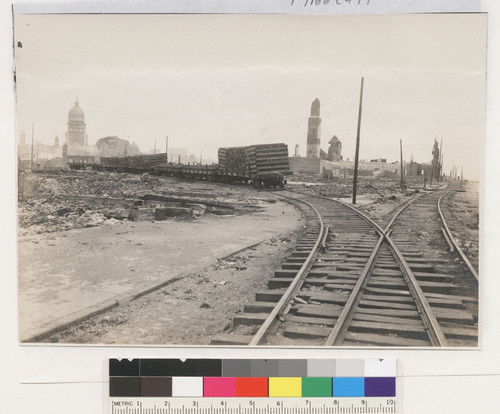 [View along railroad tracks showing cars loaded with reconstruction material (?). From near Howard and Eleventh Sts. City Hall in distance, left.]