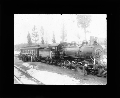 Railroad train with passengers standing beside in the snow, lantern slide