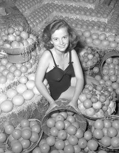 Portrait of a girl in a bathing suit sitting among baskets of oranges for a produce exhibition