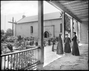 Two priests and a monk (or a nun?) chatting in the courtyard of the Plaza Church (near the chapel?), Los Angeles, 1885